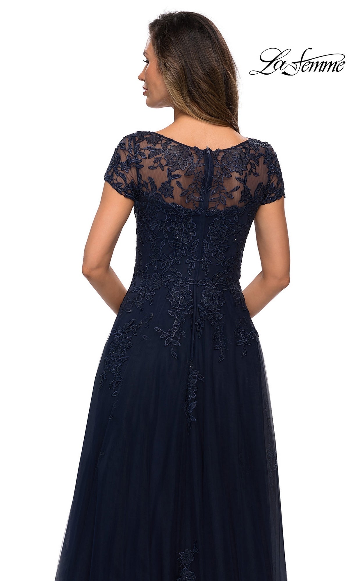 Woman facing away in a navy blue Long Formal Dress: La Femme 27920 with an A-line silhouette, short lace sleeves, and floral lace bodice. “La Femme” logo top right.